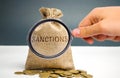 A magnifying glass is looking at a money bag with the word Sanctions. The imposition of economic and political sanctions on the