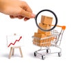 Magnifying glass is looking at the Supermarket cart with boxes and a graph with red arrow, merchandise: the concept of buying Royalty Free Stock Photo