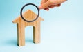 Magnifying glass is looking at the Wooden house on a blue background. Lending to the public. The concept of affordable housing