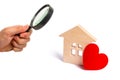 Magnifying glass is looking at the Wooden house with a red heart on a white background. Affordable housing. Family psychology. Royalty Free Stock Photo