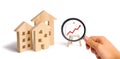 Magnifying glass is looking at the Wooden houses stand with red arrow up. Growing demand for housing and real estate. The growth o Royalty Free Stock Photo