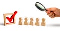 Magnifying glass is looking at the wooden human figures stand in a row next to wooden tick in the box. concept of elections