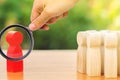 A magnifying glass looks at a red figurine of a man stands aside from the crowd of people. Asociality, sociopathy