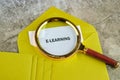 A magnifying glass rests on a yellow envelope that contains a document titled E LEARNING. The scene captures the essence