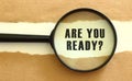 The magnifying glass reveals the ARE YOU READY text appearing behind the torn brown paper. Royalty Free Stock Photo