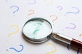 Magnifying glass on sheet of paper with question marks. Search Royalty Free Stock Photo