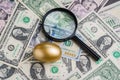 Magnifying glass with shiny golden egg under pile of US America dollar banknotes money metaphor of precious wealth, finding good Royalty Free Stock Photo