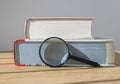 Magnifying glass with stack of close thick books on wooden table with day light