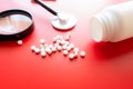 Magnifying glass, tablets and bottle on red reflection background. Checking ingredients and effectiveness of medicine Royalty Free Stock Photo