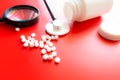 Magnifying glass, tablets and bottle on red reflection background. Checking ingredients and effectiveness of medicine Royalty Free Stock Photo