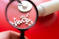 Magnifying glass, tablets and bottle on red reflection background. Checking ingredients and effectiveness of medicine Royalty Free Stock Photo