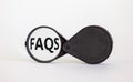 Magnifying glass with text `FAQS` on beautiful white background. Business concept, copy space