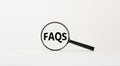 Magnifying glass with text `FAQS` on beautiful white background. Business concept, copy space