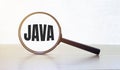 Magnifying glass with text JAVA on wooden table