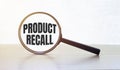Magnifying glass with text Product Recall on wooden table