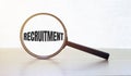 Magnifying glass with text RECRUITMENT on wooden table