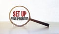 Magnifying glass with text SET UP YOUR PRIORITIES on wooden table