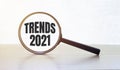 Magnifying glass with text TRENDS 2021 on wooden table