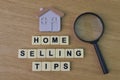 Magnifying glass, toy house and square letters with text HOME SELLING TIPS over wooden background