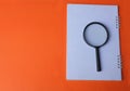 Top view a magnifying glass on a white book on orange paper background