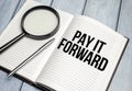 magnifying glass and a white notebook with the text we PAY IT FORWARD Royalty Free Stock Photo