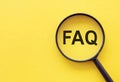 Magnifying glass on wood letters as FAQ abbreviation, frequently asked questions on yellow background