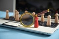 Magnifying glass, wooden human figures on laptop keyboard. Candidate selection