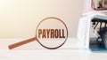 Magnifying glass with the word PAYROLL on office table