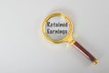 Magnifying glass written with RETAINED EARNINGS isolated on a grey background