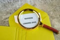 A magnifying lens rests upon a bright yellow envelope, focusing on a paper displaying Success Loading 2026. Several other Royalty Free Stock Photo