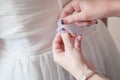 A maid of honor assists with tying the bride`s ribbon sash on her gown.