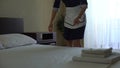 Maid in hotel laying clean towel down and smoothing bed sheets, HoReCa service