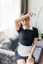 Maid in white apron sitting on sofa and wiping forehead with closed eyes Royalty Free Stock Photo