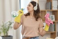 Maid woman, bottle and singing with headphones, cloth and happy with music, dancing and audio streaming. Cleaner girl