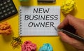 Mail hand writing `new business owner` on white note, beautiful yellow background, colored paper clips, metalic pen, cap and Royalty Free Stock Photo