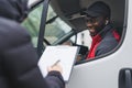 Mail and post packages concept. Unrecognizable person in black jacket signing delivery documents next to white truck