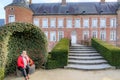 Main facade of 16th century Alden Biesen castle, smiling adult female tourist sitting next to her dog