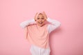 Main focus on facial expression of Muslim woman in pink hijab holding her head with hands, smiling with toothy smile looking at Royalty Free Stock Photo