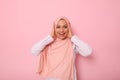 Happy religious Muslim woman in pink hijab holding her head with hands and smiling with toothy smile looking at camera with Royalty Free Stock Photo