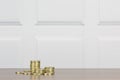 Stacks of gold coloured coins on a wooden surface with soft white panel background