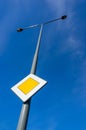 Main road traffic sign on a street lamp against the blue clear sky Royalty Free Stock Photo