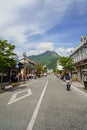 Main road from train station filled with people, streetscape and shops direct to fresh green Yufudake mountain peak, blue sky Royalty Free Stock Photo