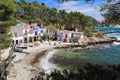 Main view of cala s`Alguer, a lovely beach surrounded by traditional fishermen`s white buildings with colorful doors and windows.