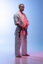 Side view full-length portrait of young professional karate, judo sportsman in white kimono isolated over gradient white