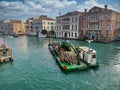 A maintenance barge carrying a supply of wooden pilings moves along a canal in central Venice, Italy on a cloudy day in Autumn
