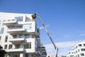 Maintenance workers working at heights from an articulated boom lift, repairing facade of residential building.