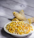 Maize-cob and yellow corn kernels in white glass vase on white wooden background- zea mays Royalty Free Stock Photo