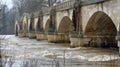 The majestic arches of an ancient bridge ly visible under the rushing floodwater representing both the engineering