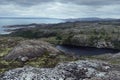 Majestic cold arctic black granite mountains with green lichen, moss, dark lake and grey Arctic Ocean in cloudy weather, arctic.