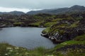 Majestic cold arctic black granite mountains with green lichen, moss and swamp, dark lake and low grey clouds in rainy weather.